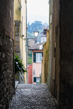 View of a narrow cobblestone alleyway with historic stone walls and a vintage street lamp in the charming town of Varenna, Lombardia, Italy.