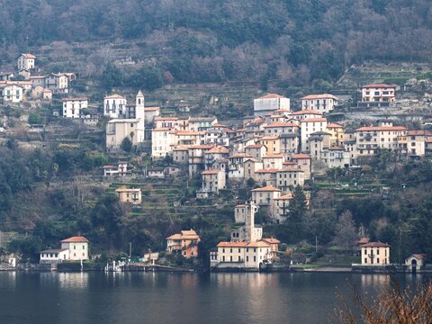 View of the historic village of Varenna nestled on the shores of Lake Como, featuring traditional stone buildings, terraced hillsides, and a church tower, Varenna, Lombardia, Italy.
