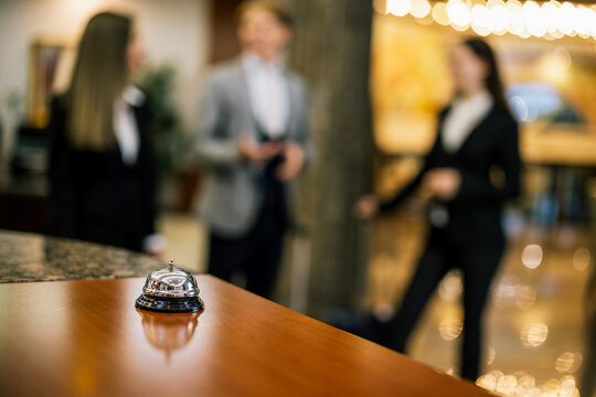 Close-up of a hotel bell on a luxury reception desk with people in background