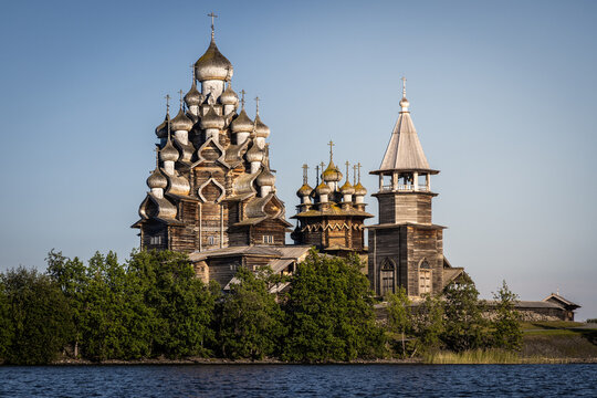 View of the historic wooden Kizhi Pogost church with its iconic multiple domes, surrounded by lush green trees on the shore of Lake Onega in Petrozavodsk, Republic of Karelia, Russia.