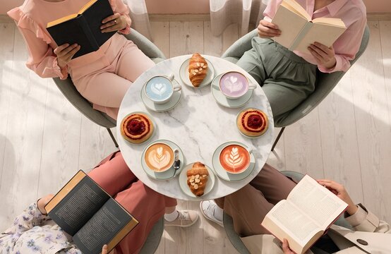 Coffee cups with latte art pastries and open books arranged on round table symbolizing social reading club atmosphere relaxation culture and shared knowledge generated ai