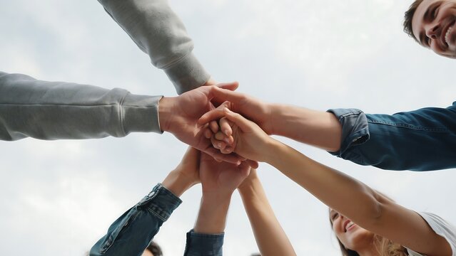 Group of people joining hands together in a circle showing unity and teamwork under bright sky