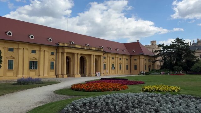 Visitors walk through the landscaped gardens in front of Lednice Castle on a sunny day in the Czech Republic. Historic architecture, cultural heritage, sightseeing, tourism and European travel destina