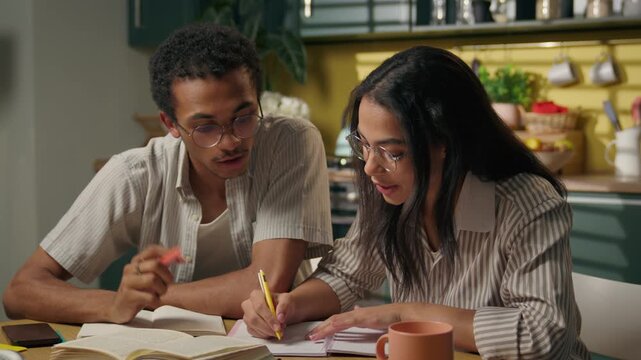 Thoughtful African American man and Latino woman studying together at home brainstorming idea pupils writing task teamwork friends giving high five multiracial teenagers education solutions at kitchen