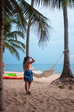 View of a woman standing on the sandy beach under palm trees with a hammock and kayaks nearby in Phu Quoc, Kien Giang, Vietnam.