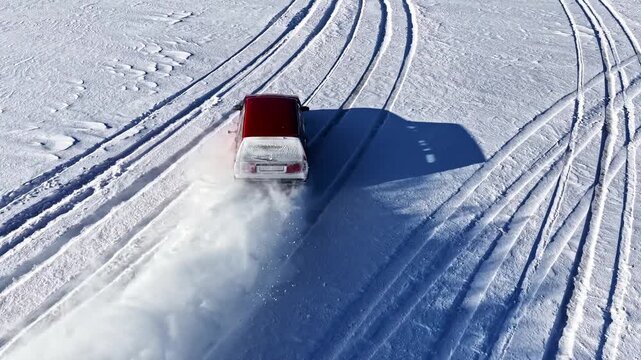 Aerial view of a car drifting on a snow-covered field, creating tire tracks and kicking up snow in Latvia.