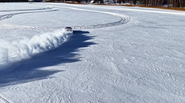 Aerial view of a car performing a drift maneuver on a frozen lake surrounded by snow-covered forest in Latvia.