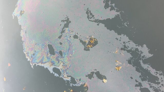 Iridescent oil slick polluting dark water surface