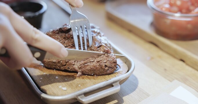 Hands cutting grilled steak on wooden board