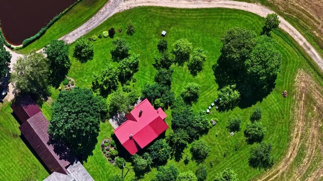 Aerial view of a house with a red roof surrounded by lush green trees and a grassy lawn in a rural landscape in Riga, Latvia.