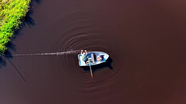 Aerial view of two fishermen in a small boat casting a fishing net into the dark water of a river in Riga, Latvia.