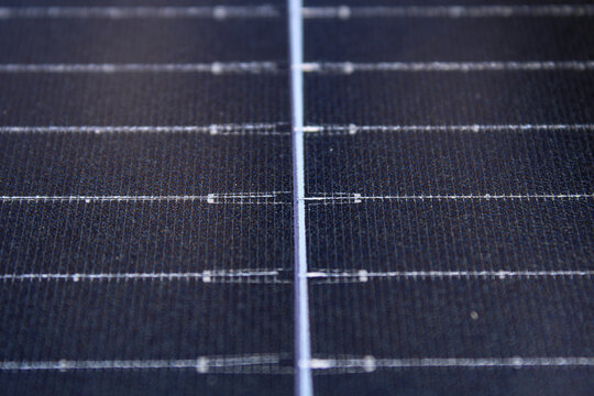 Close-up of a solar panel surface featuring textured dark blue cells and silver grid lines, showcasing renewable energy technology with selective focus.