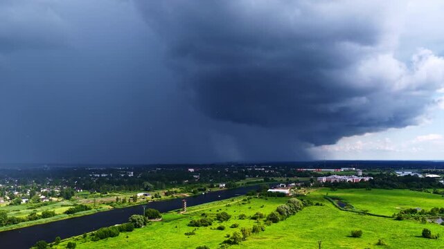 Aerial view of a dark storm front approaching over the green landscape and river in Riga, Latvia.