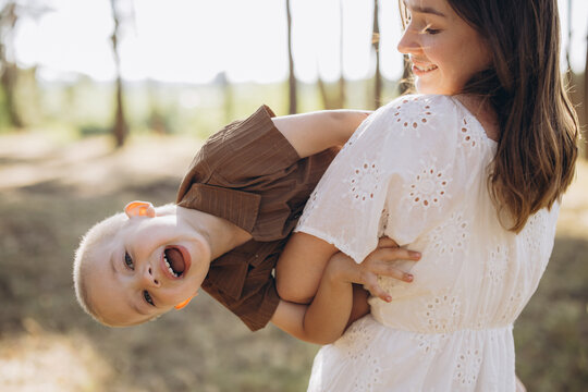 Mother holding and playing with happy son upside down outdoors, enjoying summer family time and fun