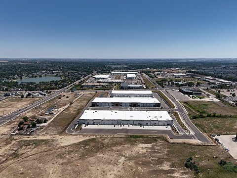 Aerial view of modern industrial warehouses with white roofs surrounded by paved roads and open land in Thornton, Colorado, United States.