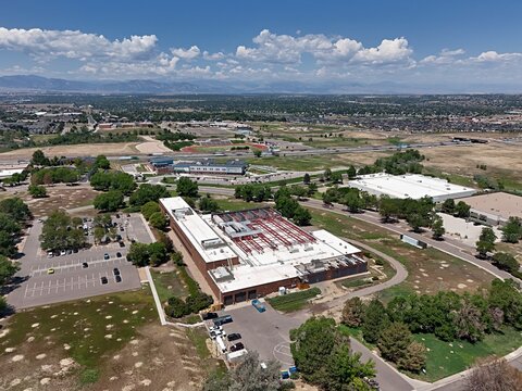 Aerial view of a large commercial building with a flat roof and parking lot surrounded by open fields and suburban development in Thornton, Colorado, United States.