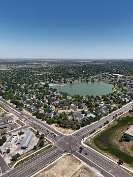 Aerial view of a suburban neighborhood surrounding a central lake with a large road intersection and residential houses in Thornton, Colorado, United States.