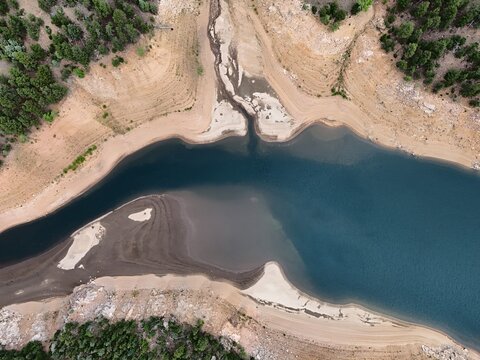 Aerial view of Gross Reservoir showing the low water levels exposing the sandy shoreline and surrounding pine forest in Boulder County, Colorado, United States.