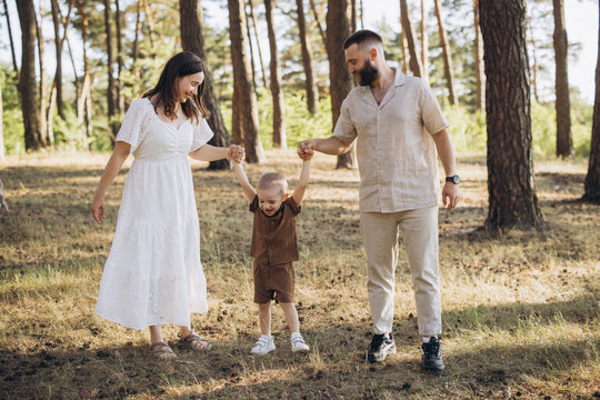 Happy family holding hands enjoying summer walk in nature forest with young son learning to take steps