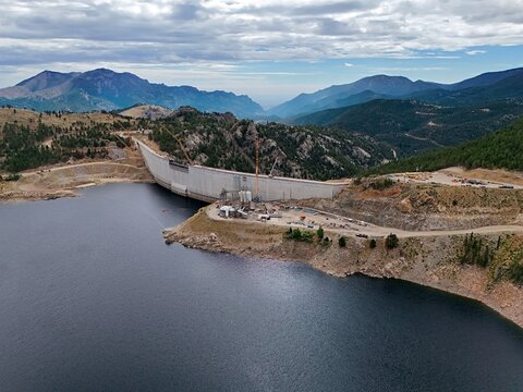 Aerial view of the Gross Reservoir dam construction site featuring the concrete wall, surrounding mountainous terrain, and reservoir water in Boulder County, Colorado, United States.