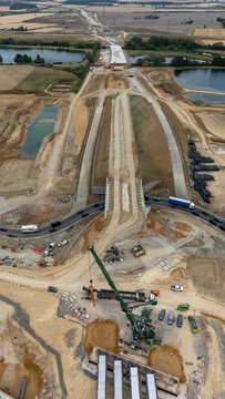 Aerial view of the Black Cat Roundabout construction site featuring heavy machinery, a large crane, ongoing road works, and surrounding fields in Chawston, England, United Kingdom.