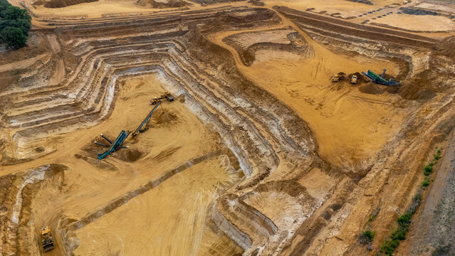 Aerial view of a large sand quarry with heavy machinery and excavators operating within the terraced excavation site in Sandy, England, United Kingdom.