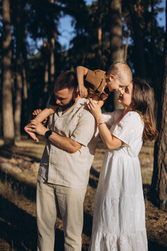 Family enjoying summer day in forest, father carrying son on shoulders, mother looking at child