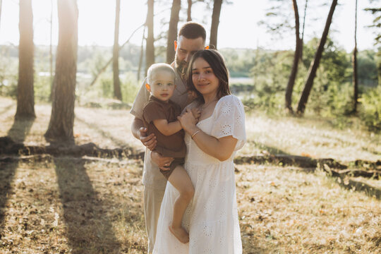 Young family enjoying summer activity in the forest, parents holding their son, togetherness and love at sunset