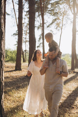 Obraz premium Happy family with child on shoulders walking in summer forest during golden hour, enjoying leisure time outdoors