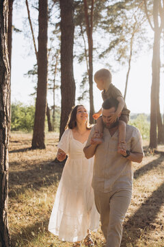 Happy family with child on shoulders walking in summer forest during golden hour, enjoying leisure time outdoors