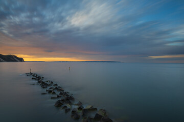 Fototapeta premium Rock breakwater stretching into smooth calm sea under vibrant sunset sky during twilight