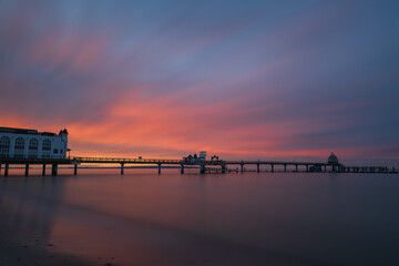 Obraz premium Historic Sellin pier resort building and walkway silhouetted against glowing orange sunset sky