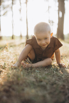 Young boy crawling on grass barefoot, exploring nature during a golden hour summer day outdoors