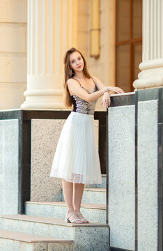 An elegant young woman in a stylish outfit poses on the stairs of a classic old building with columns. A fashion portrait, beauty, luxurious lifestyle, confidence, and urban elegance.