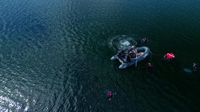 Aerial view of scuba divers preparing to dive from a small inflatable boat on the calm surface of a lake in Latvia.