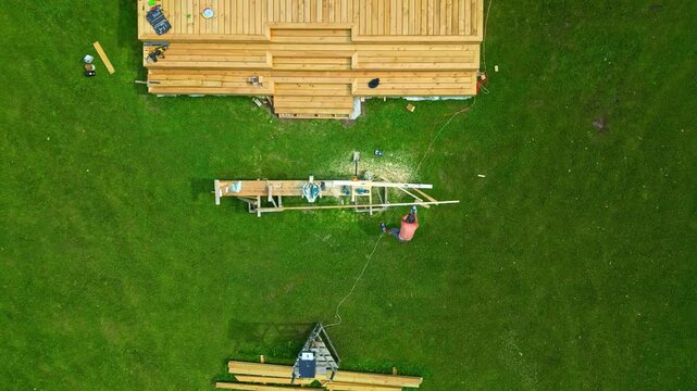 Aerial view of a carpenter working on a wooden deck construction project in a grassy field in Latvia.