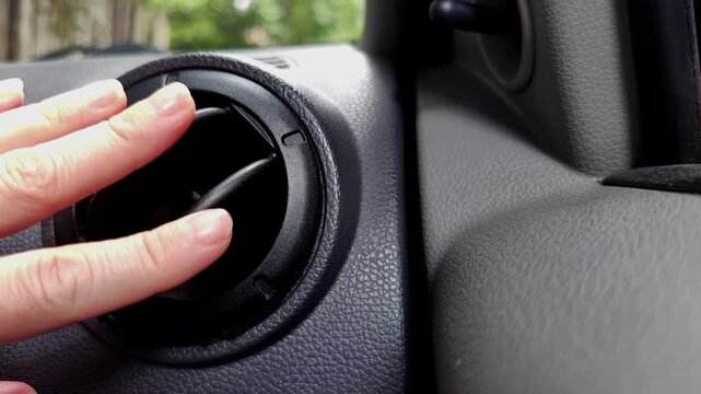 Woman closes a black dashboard air vent inside a gray car interior, vehicle controls, automotive design, transportation concept, modern cabin.