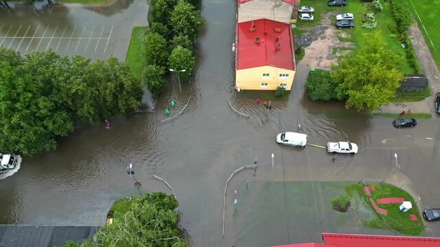 Aerial view of a flooded street intersection with vehicles navigating through deep water near residential buildings in Latvia.