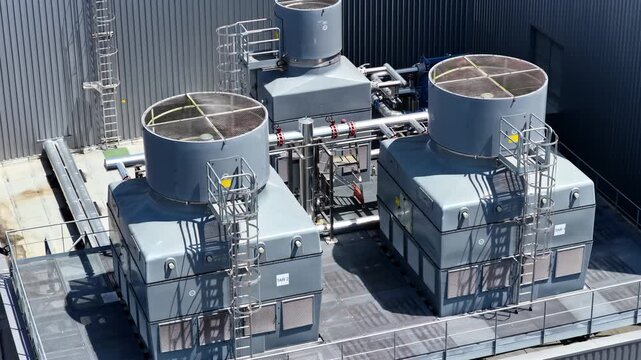 Aerial view of industrial cooling towers on a rooftop with metal piping and ventilation fans in France.