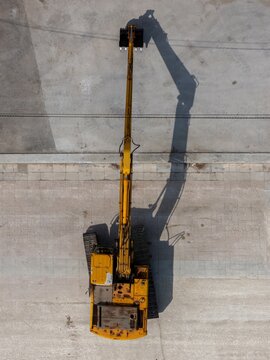 Aerial view of yellow excavator on a paved construction site with long shadow cast on the ground in Alges, Lisbon, Portugal.