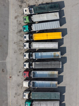 Aerial view of a row of colorful long haul trucks parked in a line on a paved lot in Alges, Lisbon, Portugal.