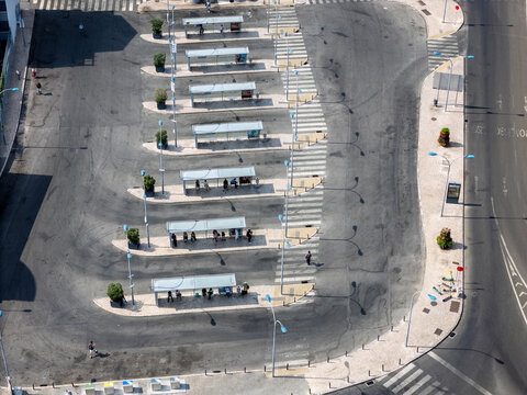 Aerial view of the bus terminal with multiple shelters, people waiting, and paved lanes in Alges, Lisbon, Portugal.