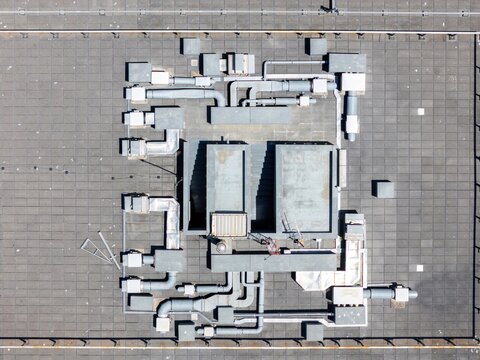 Aerial view of a flat rooftop featuring complex HVAC ventilation systems, metal pipes, and industrial ductwork in Cascais, Lisbon, Portugal.
