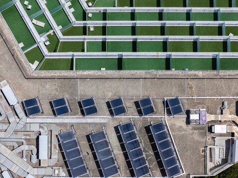 Aerial view of solar panels installed on a flat rooftop next to green terrace areas with lounge chairs in Cascais, Lisbon, Portugal.