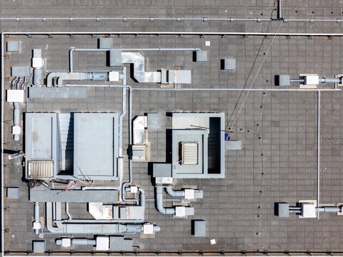 Aerial view of a flat rooftop featuring various HVAC ventilation systems, metallic pipes, and industrial equipment in Cascais, Lisbon, Portugal.