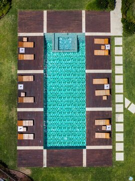 Aerial view of a rectangular swimming pool with turquoise water surrounded by a wooden deck with sun loungers set in a lush green garden in Cascais, Lisbon, Portugal.