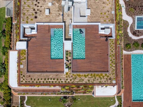 Aerial view of a modern building featuring two rooftop swimming pools with wooden decking and lush green roof landscaping in Cascais, Lisbon, Portugal.