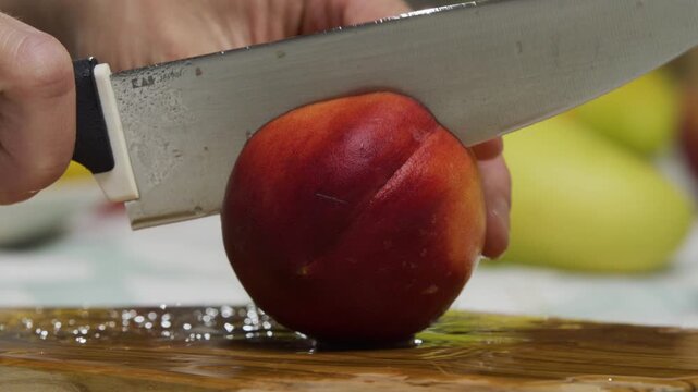 Knife cutting through peach and person breaking it into two - closeup shot
