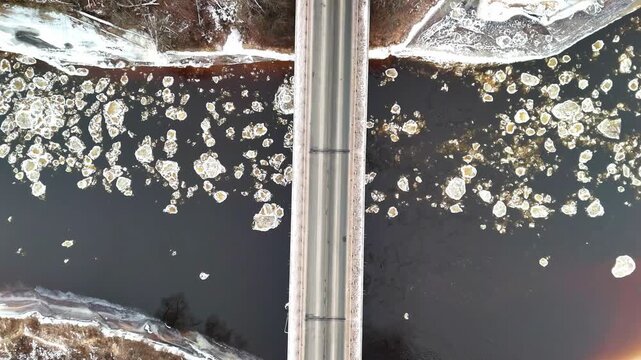 Aerial view of a bridge spanning a river filled with floating ice chunks during winter in Riga, Latvia.
