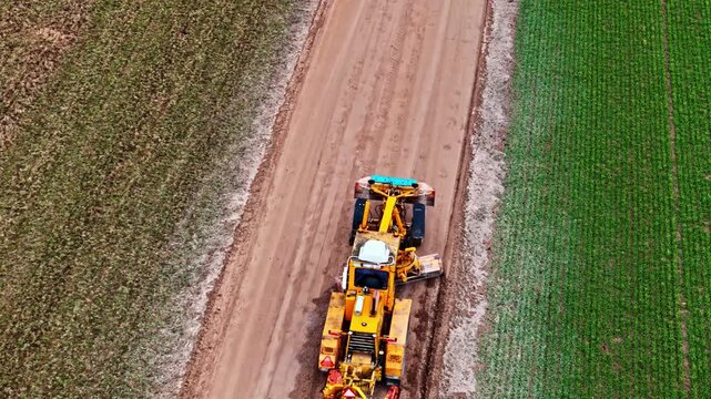 Aerial view of a yellow motor grader working on a dirt road between agricultural fields in Riga, Latvia.